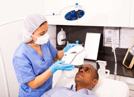 Male client getting face phototherapy procedure in clinicの写真素材