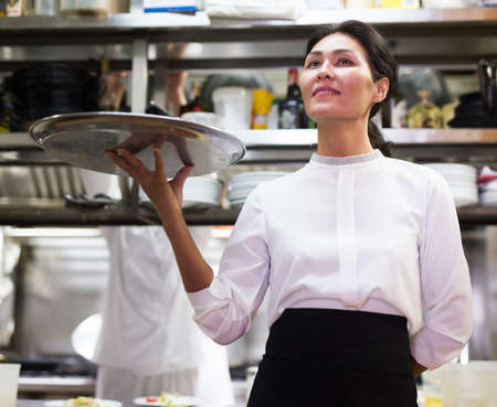 portrait of smiling female waiter standing in kitchen in restauranteの写真素材