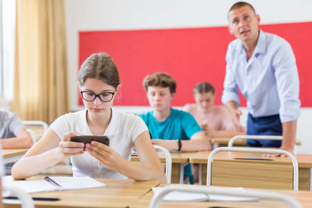 Teenager students sitting in class room with smartphonesの写真素材