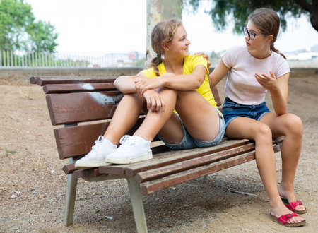 Best friends chatting while sitting on bench in parkの写真素材