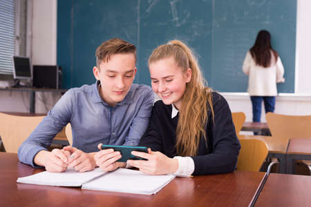 Cheerful teenagers with phone in schoolroomの写真素材