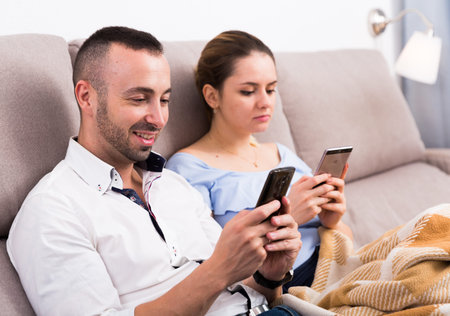 Man ans his wife are chatting on phone in time resting on sofa
