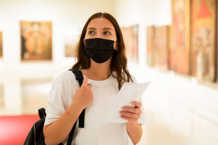 Young girl in a protective mask visits an exhibition of paintings in a museumの写真素材
