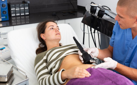 Cosmetologist performing ultrasound cavitation body procedure for female clientの写真素材