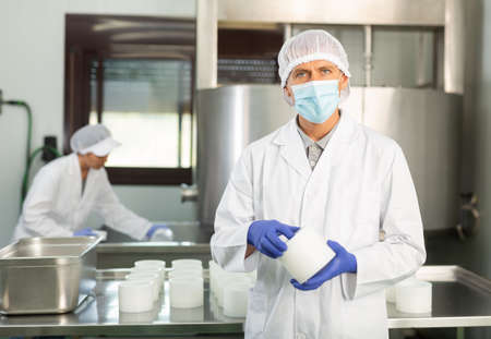Worker in white coat and in protective mask working at cottage cheese production on factoryの写真素材
