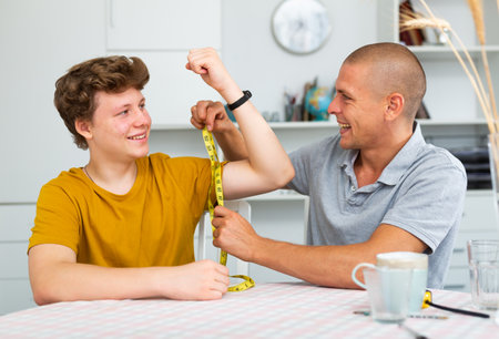 Father measuring son biceps with measuring tapeの写真素材