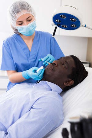 Female beautician injecting facial filler to male client in clinicの写真素材