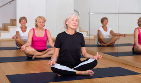 Aged woman meditating in yoga position Padmasana during group trainingの写真素材