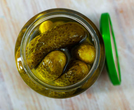 Glass jar with pickled cucumbers on a wooden tableの写真素材