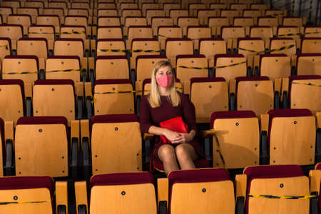 Reflective woman in protective mask sitting alone in empty cinema houseの写真素材