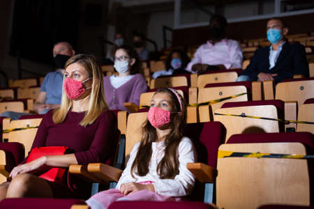 Woman with preteen daughter in masks watching theatrical performanceの写真素材