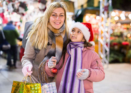 Joyous mother with little daughter buying decorations for Xmas at an marketの写真素材