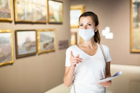 Woman in mask observing artworks in museumの写真素材