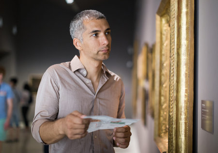 Adult male is visiting at the pictures exposition with brochure