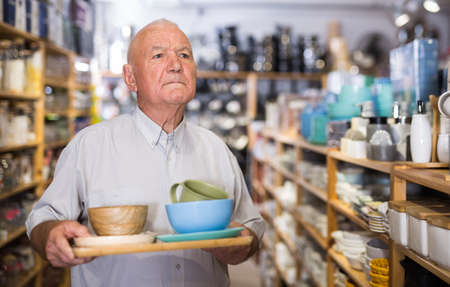 Senior man customer holding purchases and walking in household goods storeの写真素材