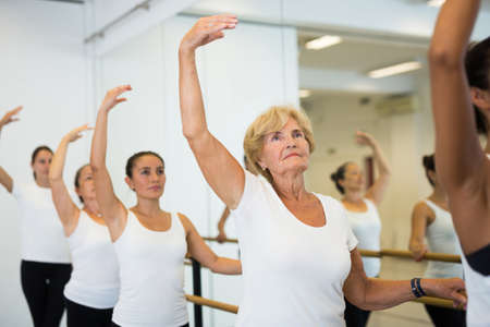 Group of ballerina standing with one hand on barre and reaching over hand in fitness roomの写真素材