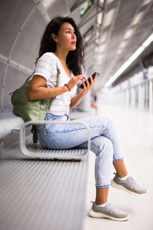 Woman using smartphone while waiting for train in metro stationの写真素材
