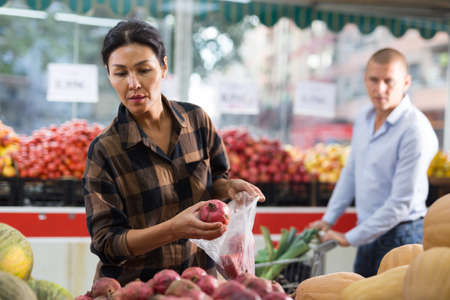 Woman selecting pomegranate in greengrocerの写真素材