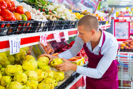 Supermarket worker putting quinces on shelfの写真素材