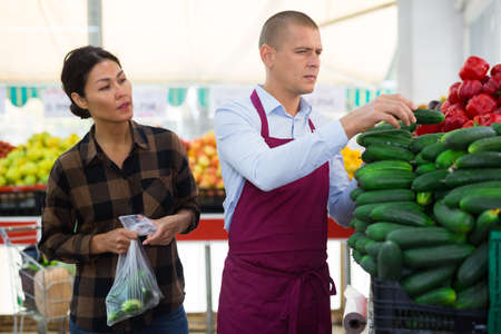 Greengrocer worker helping woman to choose cucumbersの写真素材