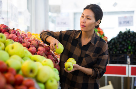 Asian woman choosing apples on counter of farmers marketの写真素材