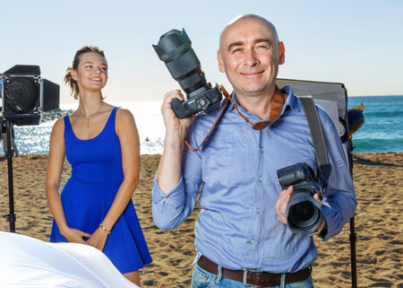 Portrait of male photographer with camera among professional photo equipment on seaside
