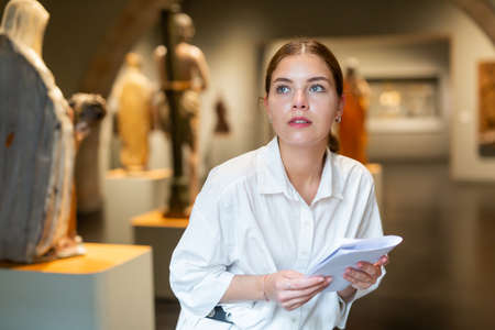 Woman visiting sculpture hall in museum and looking at exhibitsの写真素材