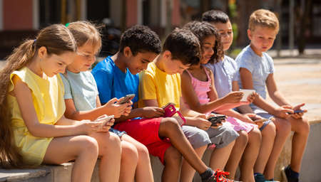 Children chatting on their smartphone, sitting on parapetの写真素材