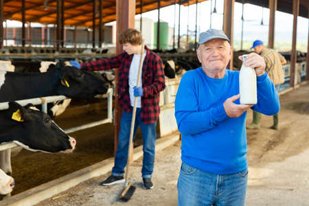 Positive aged man dairy farm owner holding bottle of milkの写真素材