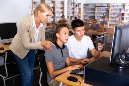 Schoolboys using computer and teacher helping to him in classroomの写真素材