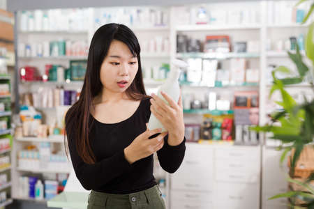 Positive chinese woman near counter chooses antibacterial at in pharmacyの写真素材
