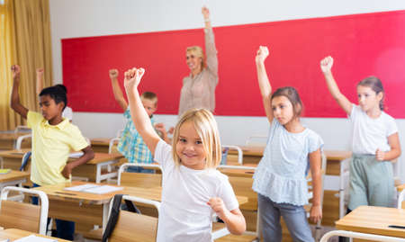 Teacher conducts gymnastics for elementary school children in classroomの写真素材