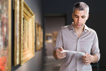 Adult male is visiting at the pictures exposition with brochureの写真素材