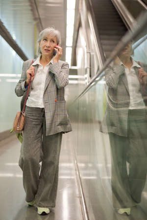 Mature woman walking in mall and talking on phoneの写真素材