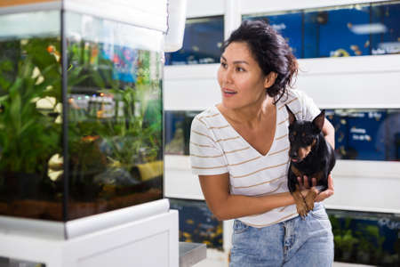 Woman with dog looking at aquarium in pet shopの写真素材