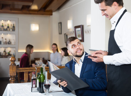 Hospitable waiter helping young male with menuの写真素材