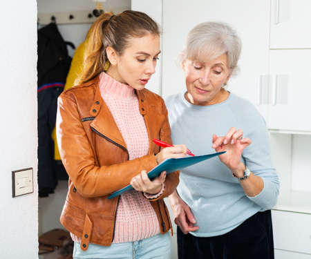 Elderly lady and younger woman filling documentation at homeの写真素材