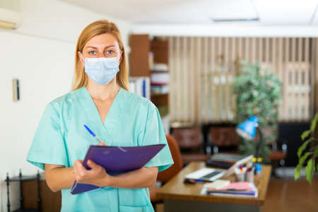 Female doctor in face mask standing in medical officeの写真素材