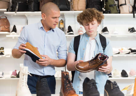 Shoe salesman helping teen to choose fashionable winter boots at shoe shopの写真素材
