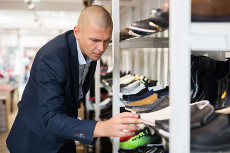Interested man choosing new shoes on shelves of shoe storeの写真素材