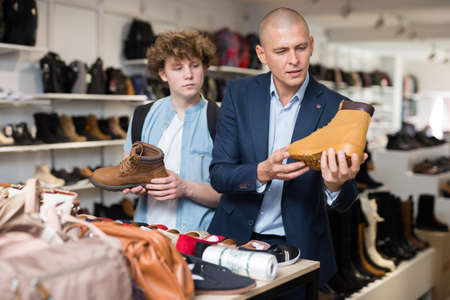 Father and son choose and buy fashionable brown winter boots in shoe storeの写真素材