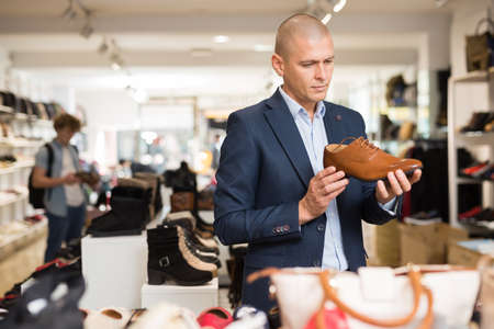 Focused man looking at brown leather dress shoe in storeの写真素材