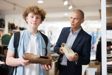 Teenager with the help of sales assistant selects summer shoesの写真素材