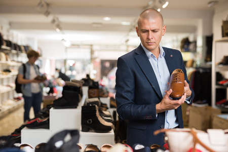 Handsome man chooses classic brown shoes in shoe storeの写真素材