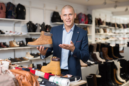 Positive man choosing fashionable winter boots in shoe storeの写真素材