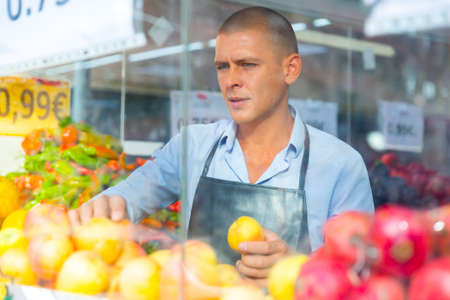 Supermarket worker setting out goods in greengrocerの写真素材
