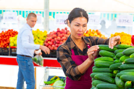 Supermarket worker putting cucumber on counterの写真素材