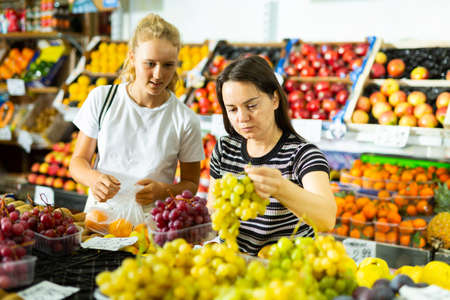 Teenage girl and her mother buying grape at groceryの写真素材
