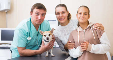Portrait of happy mother and daughter consulting by professional veterinarian about their dog healthの写真素材