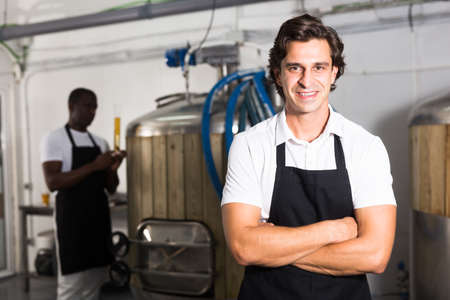 Young man brewer in uniform is standing in brew-houseの写真素材